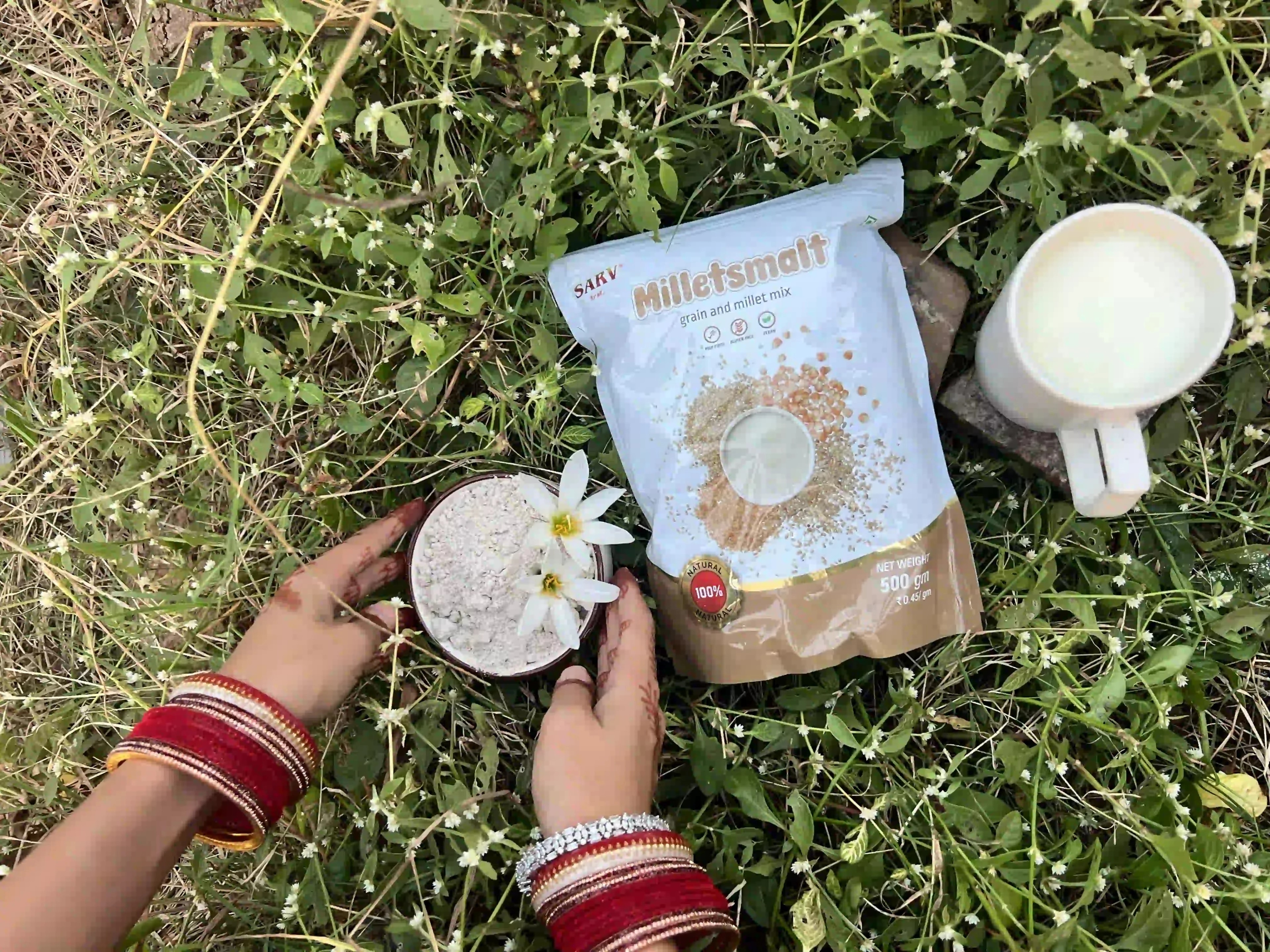 Pack of Milletsmalt grain and millet mix beside a bowl of millet flour and a cup of milk, on grass